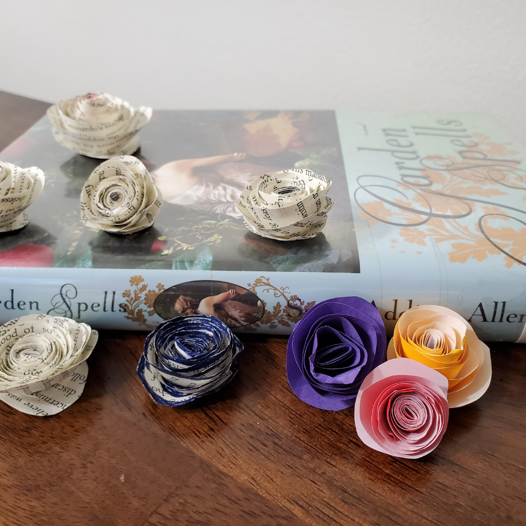 Small roses made out of old book pages and colored paper adore a copy of the book Garden Spells by Sarah Addison Allen.