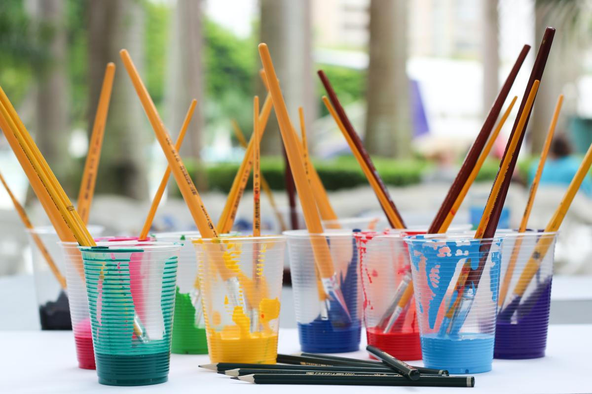 paint brushes sitting in colorful plastic cups