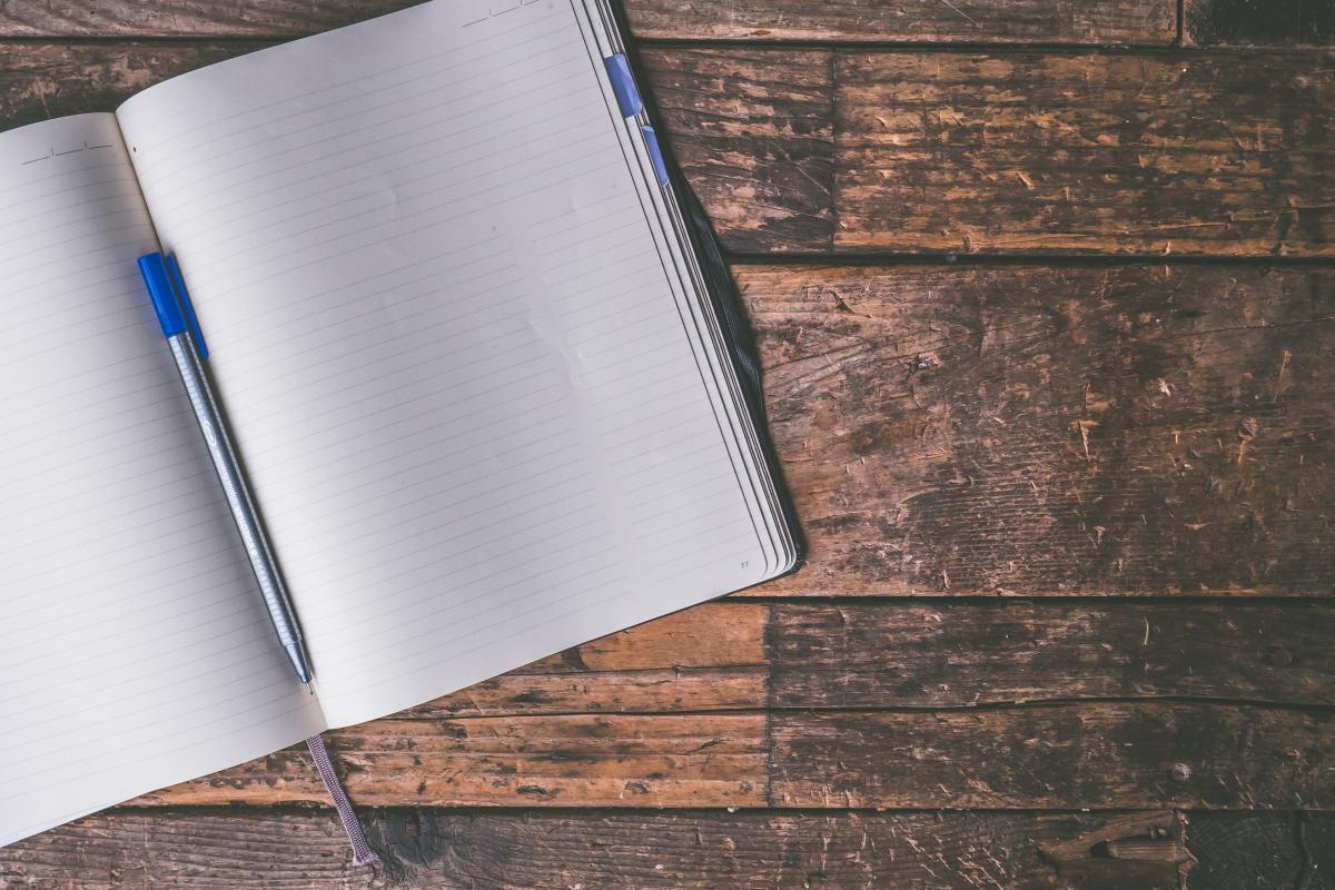 Blank notebook and pen sitting on a wooden table.