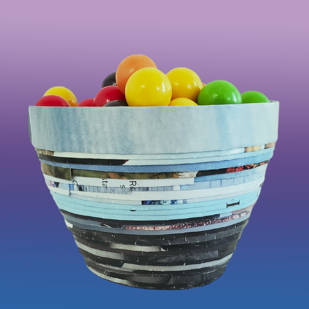 A small decorative bowl made from mostly blue and gray magazine strips. The bowl is holding Gobstoppers candy. 